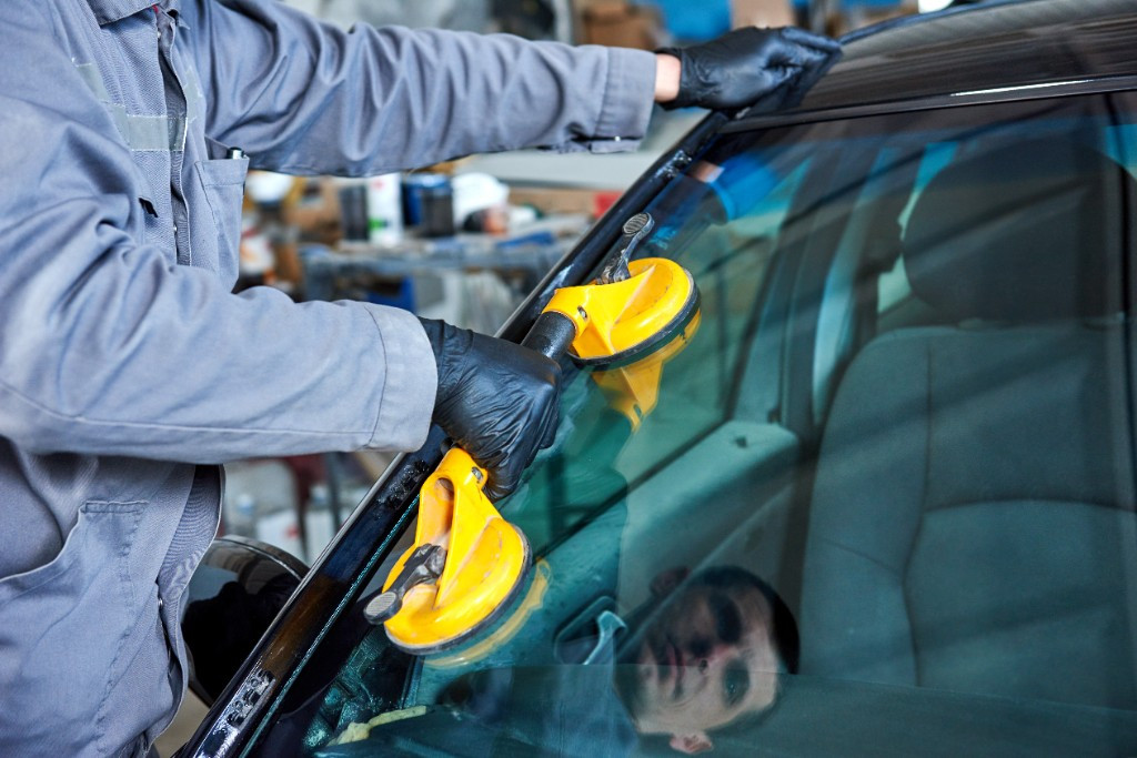 Technician using a suction-cup glass lifter to install a windshield in the shop